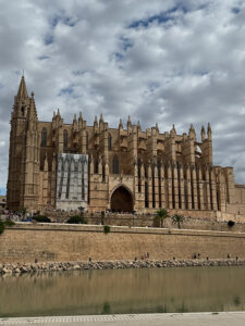 Majestic Gothic Cathedral of Santa Maria of Palma (La Seu) viewed from the Parc de la Mar pond under a cloudy sky. Part of the facade is in scaffolding.