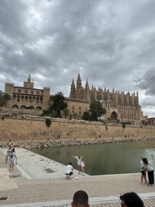 Panoramic view of the architectural complex in Palma: the Royal Palace of La Almudaina (left) and the Cathedral (right) rising above the Parc de la Mar pond. People in the foreground.