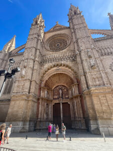 Detailed view of the main entrance to the Palma Cathedral with the large stone rose window above it. People in the foreground.