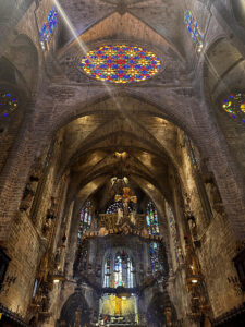 Majestic interior of the Gothic La Seu Cathedral in Palma: view of the grand stained-glass rose window (Gaudi's Eye) and the main altar. People inside.